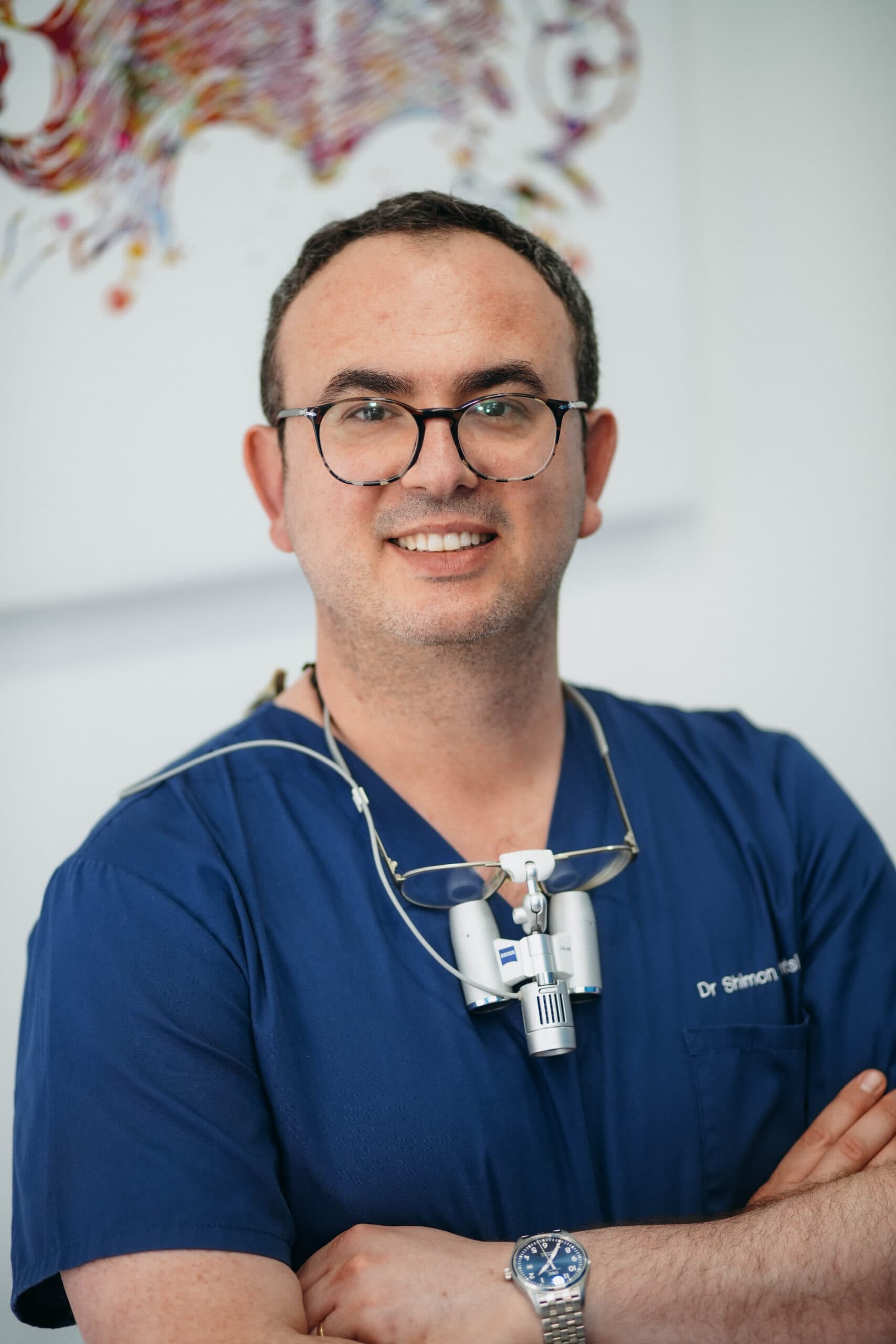 Dr Shimon Dantsis, principal dentist at London Smile Studio, in surgical scrubs with loupes around his neck.