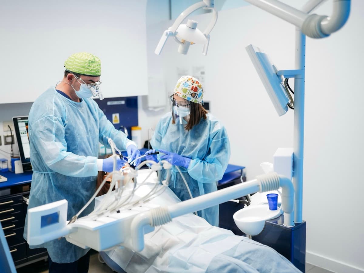 Two gowned clinicians at London Smile Studio carry out a wisdom tooth removal on a patient in the dental chair.