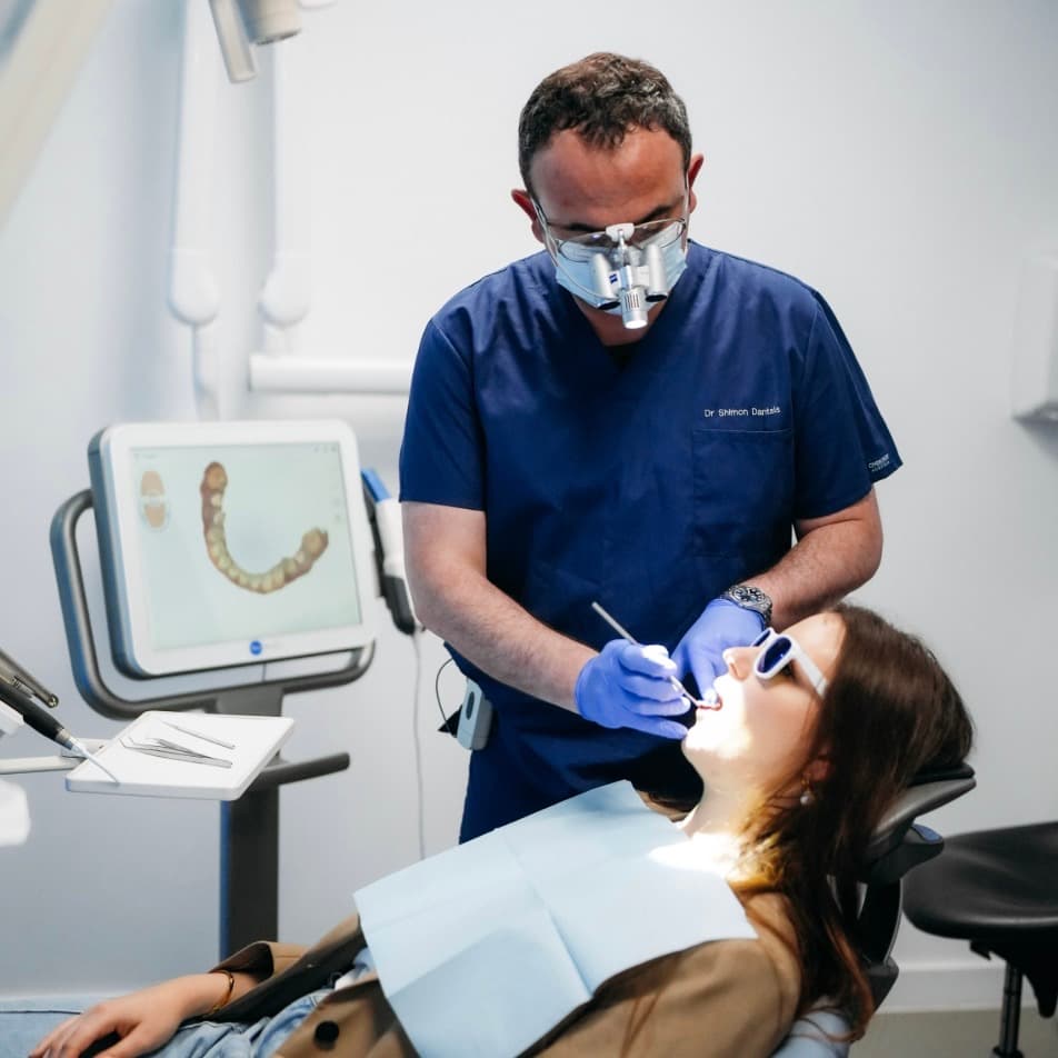 Dr Shimon Dantsis at London Smile Studio examines a patient's mouth, with a digital scan of their lower teeth visible on the monitor behind him.